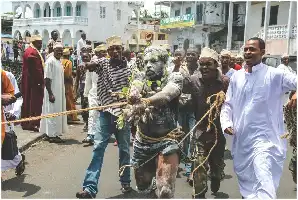 Description de l'image par IA : Défilé avec des hommes en tenue traditionnelle, l'un d'eux est attaché et recouvert de substances.