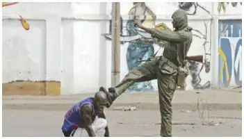Description de l'image par IA : Deux hommes jouent au football dans une rue. L'un d'eux porte un maillot bleu et tente de marquer un but contre un gardien en uniforme vert.