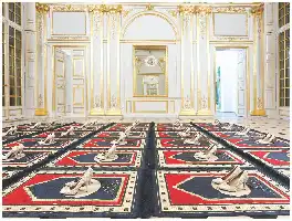 Description de l'image par IA : Salle ornée avec des chaussures sur un tapis coloré, murs dorés et fenêtres grandes.