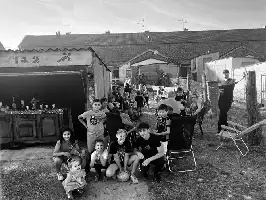 Description de l'image par IA : Groupe d'enfants et d'adultes dans un jardin, certains assis, d'autres debout, avec une table de boissons à gauche.