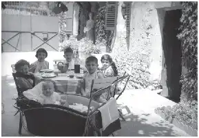 Description de l'image par IA : Six enfants assis autour d'une table en plein air, sous un auvent fleuri.