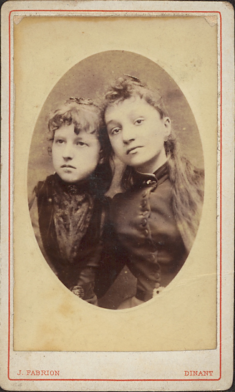 Description de l'image par IA : Deux jeunes filles posent ensemble, vêtues de robes ornées. L'une a les cheveux courts, l'autre longs.