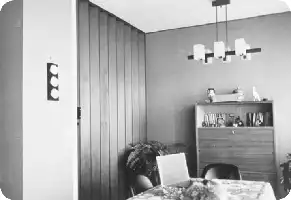 Description de l'image par IA : Une cuisine avec une cloison mobile, table longue, coin séjour avec meubles et éclairage suspendu.