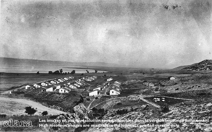 Image description generated by AI: Small village with white houses on hilly terrain, surrounded by open land and distant hills.