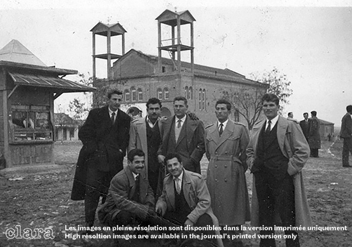 Image description generated by AI: Group of men posing in front of a church under construction. Some standing, some sitting, all dressed in suits and ties.