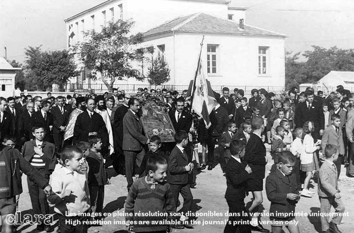 Image description generated by AI: Large group of people, including children, gathered outside a building. Some hold a flag.
