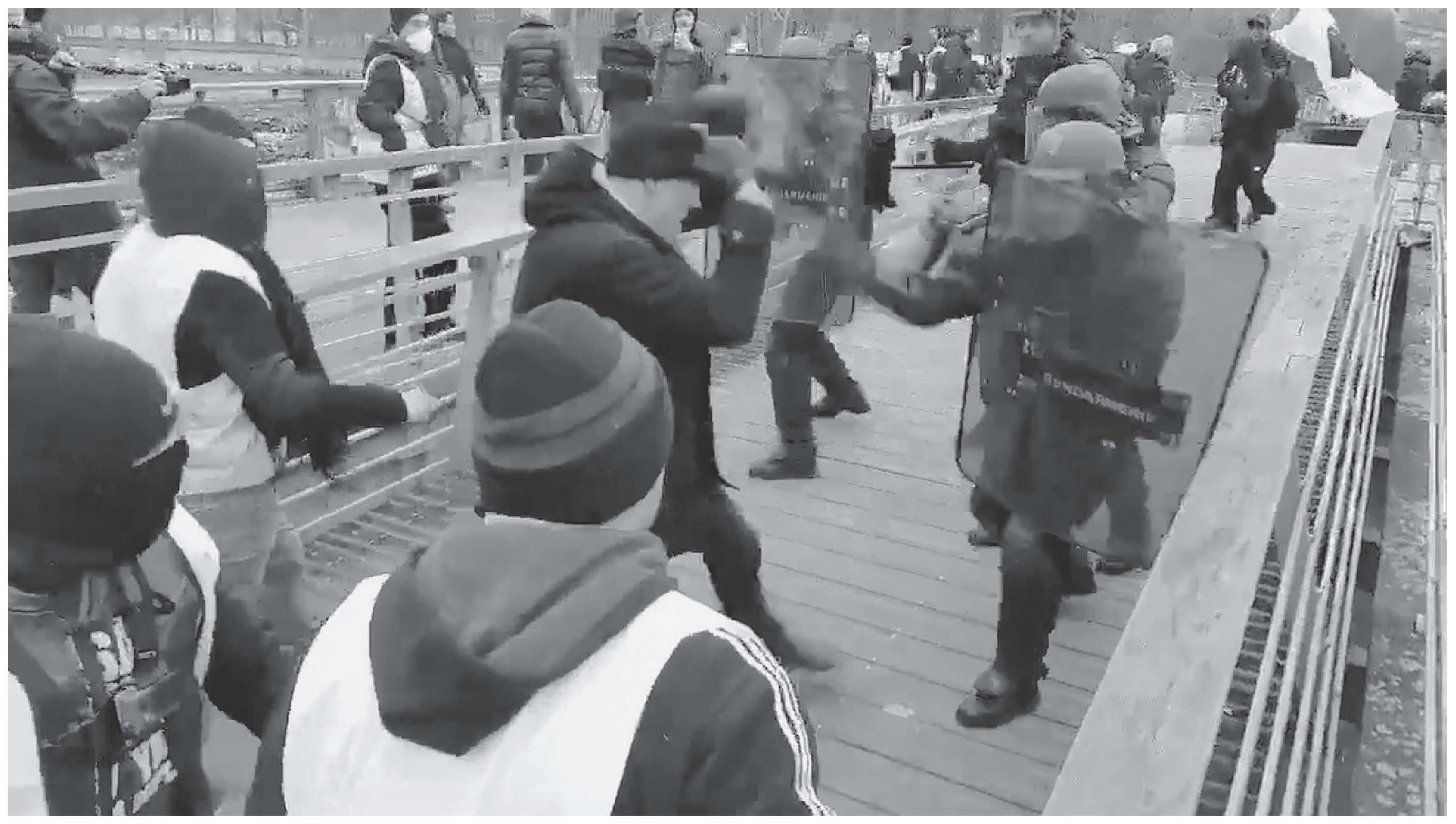 Description de l'image par IA : Des personnes en uniforme avancent sur un pont, entourées de manifestants.