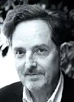 Description de l'image par IA : Homme âgé avec des cheveux gris et une barbe, portant une veste sombre, en noir et blanc.