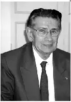 Description de l'image par IA : Homme âgé en costume et lunettes, souriant, en noir et blanc.