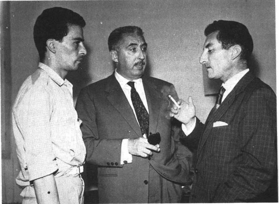 Description de l'image par IA : Trois hommes en conversation, un tenant une cigarette.