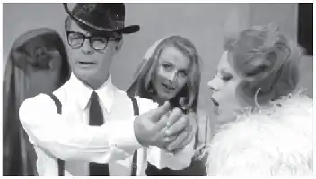 Description de l'image par IA : Trois personnes en noir et blanc. Un homme en costume et lunettes, une femme en robe de mariée, une autre en robe avec des plumes.