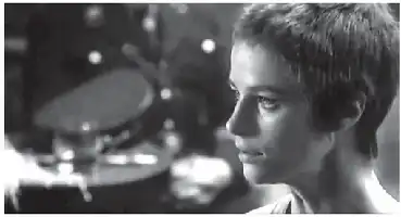 Description de l'image par IA : Jeune femme aux cheveux courts, regard sérieux, fond flou avec objets indistincts.