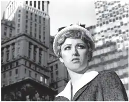Description de l'image par IA : Jeune femme en noir et blanc, chapeau avec nœud, col roulé, fond de gratte-ciel.