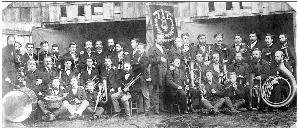 Description de l'image par IA : Groupe de musiciens, 1875. Trente-huit personnes avec instruments : fifres, cornets, clarinettes, trombones. Bannière médaillée au centre.