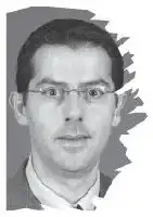 Description de l'image par IA : Homme avec des lunettes, portant une chemise blanche, regard direct.