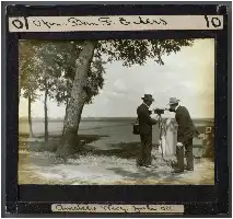 Description de l'image par IA : Deux hommes avec des chapeaux et des costumes tiennent une caméra sous un arbre, 1908.