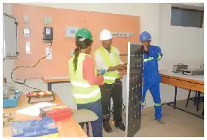 Description de l'image par IA : Trois ingénieurs en laboratoire, portant des gilets jaunes et des casques, travaillent sur un panneau solaire.
