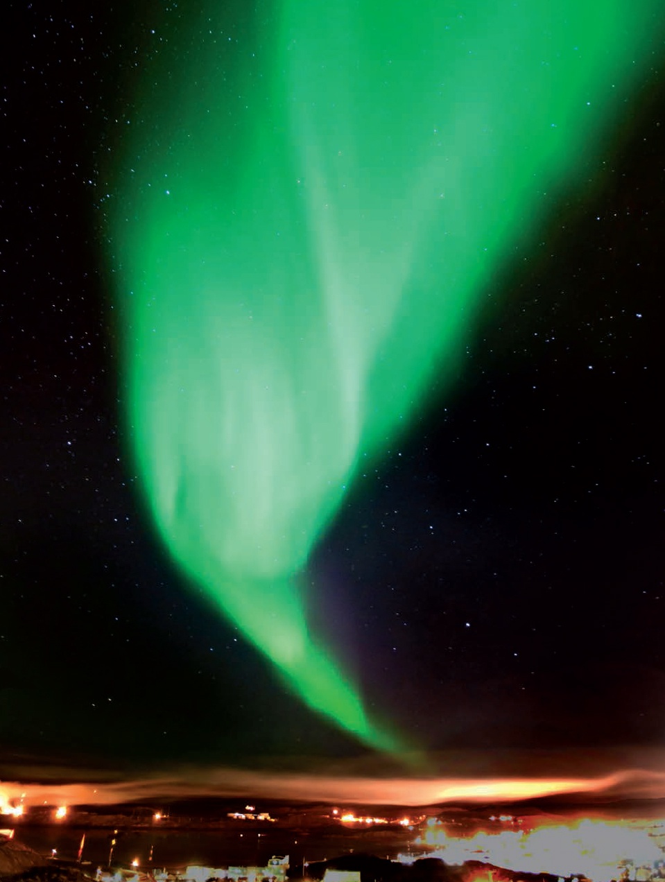 Description de l'image par IA : Aurore boréale verte vif dans le ciel nocturne, avec des étoiles et une ligne d'horizon urbaine en bas.