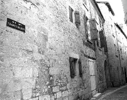 Description de l'image par IA : Rue pavée bordée de vieilles pierres, fenêtres avec volets, panneau "Rue des francs-maçons".