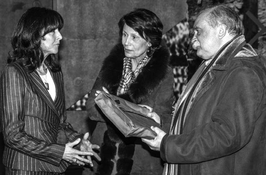 Description de l'image par IA : Trois personnes en conversation, une femme tend un document à un homme, tous vêtus de manteaux.