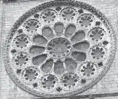 Description de l'image par IA : Rosace en pierre avec motifs floraux complexes, encadrée par des briques.