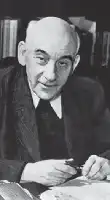 Description de l'image par IA : Homme chauve en costume, assis à un bureau, écrivant avec une plume.