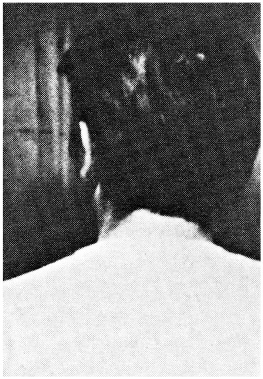 Description de l'image par IA : Femme de dos, cheveux longs, portant un foulard, assise dans une pièce sombre.