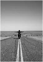 Description de l'image par IA : Motard sur une route désertique, bras tendus, en noir et blanc.