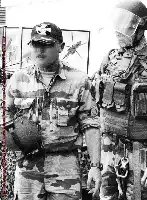Description de l'image par IA : Deux militaires en uniforme de camouflage, l'un avec un casque et une visière, l'autre avec une casquette et des lunettes de soleil.