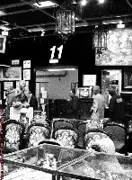 Description de l'image par IA : Salle aux enchères avec chaises ornées, tableaux et objets exposés, personnes observant les articles.