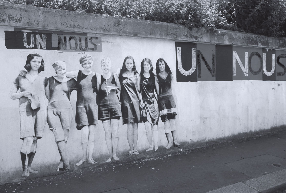 Description de l'image par IA : Six femmes en tenue des années 1920 posent devant un mur avec le mot "UN NOUS" répété.