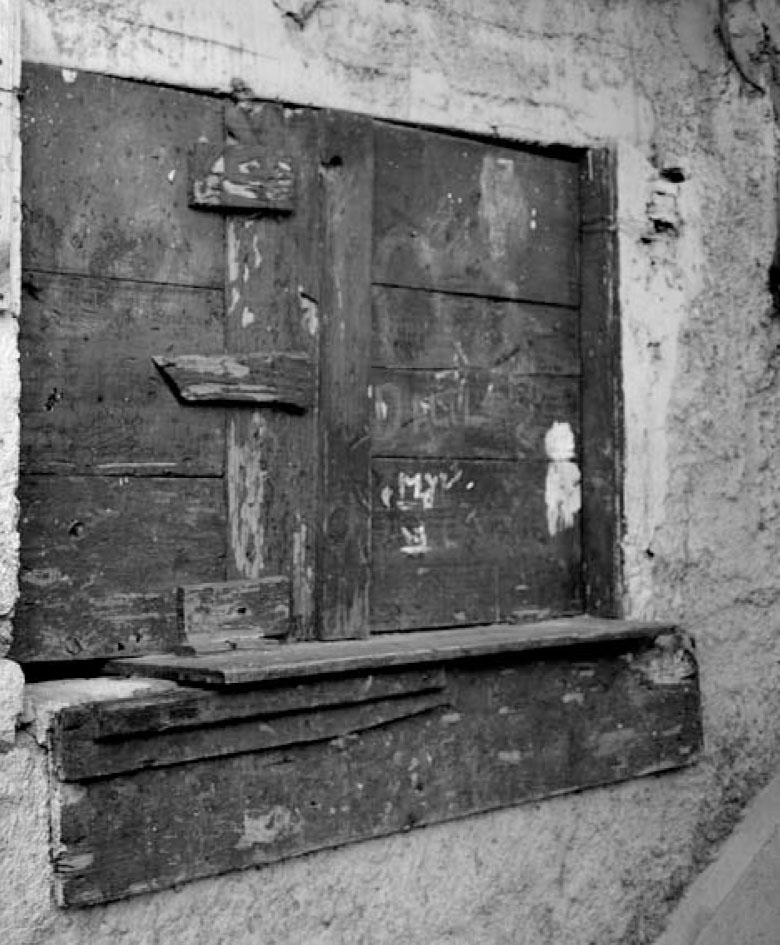 Description de l'image par IA : Porte en bois vieilli avec des marques et des loquets, encadrée dans un mur de plâtre usé.
