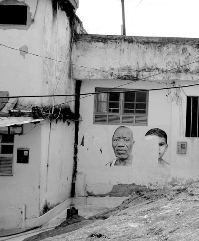 Description de l'image par IA : Bâtiment vieilli avec fresque murale de deux visages, un adulte et un enfant, sur un mur blanc.