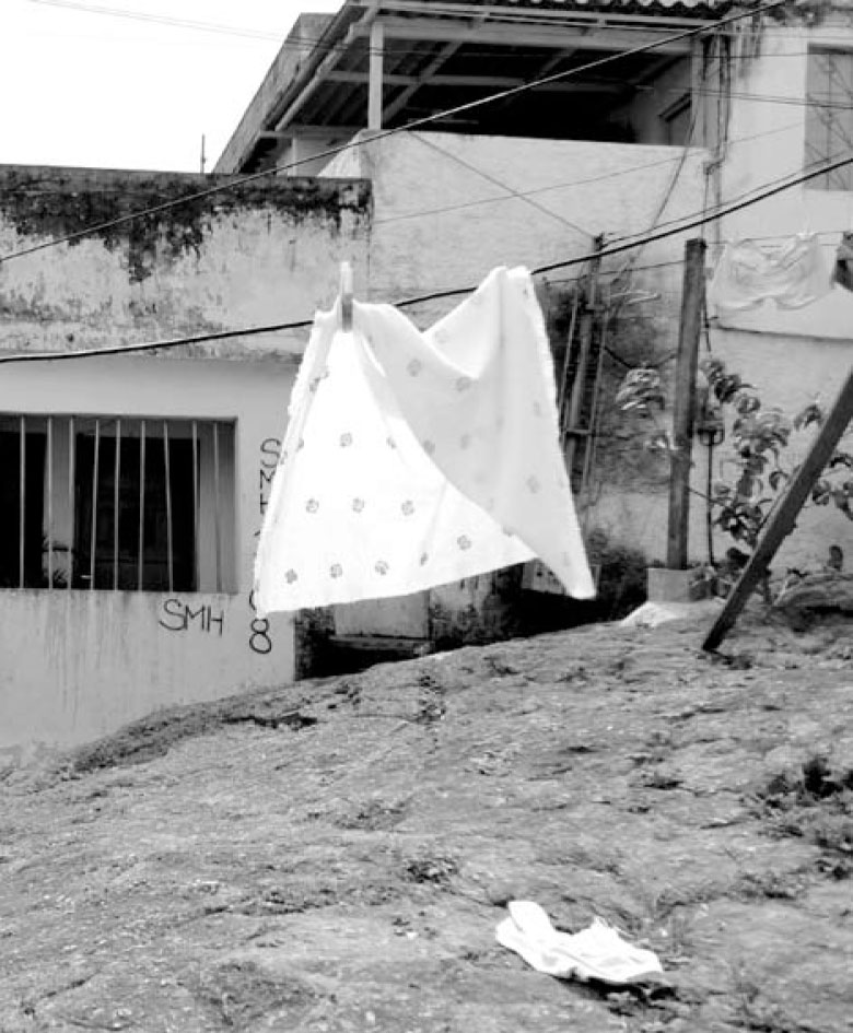 Description de l'image par IA : Une photo en noir et blanc montrant des draps étendus sur une corde à linge devant un bâtiment délabré.