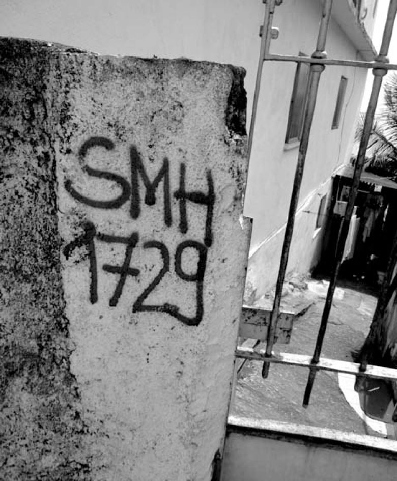 Description de l'image par IA : Pilier en béton avec inscription "SMH 1729". Vue en noir et blanc d'une rue avec grillage.