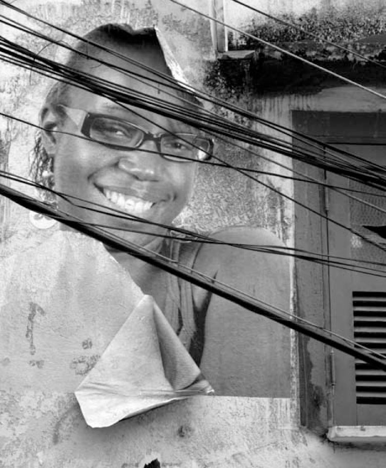 Description de l'image par IA : Portrait en noir et blanc d'une personne souriante avec des lunettes, entourée de fils électriques.
