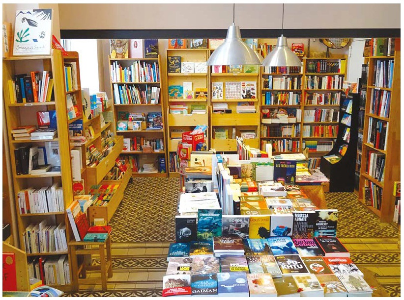 Description de l'image par IA : Bibliothèque avec des étagères remplies de livres, éclairage chaleureux, et livres exposés sur une table au centre.