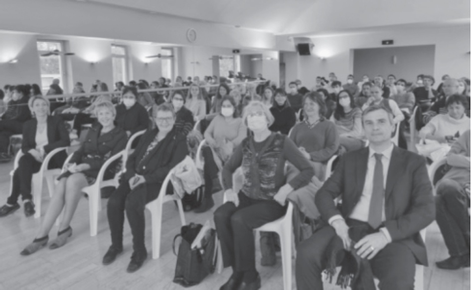 Description de l'image par IA : Salle de conférence avec de nombreux participants assis sur des chaises, certains portant des masques.