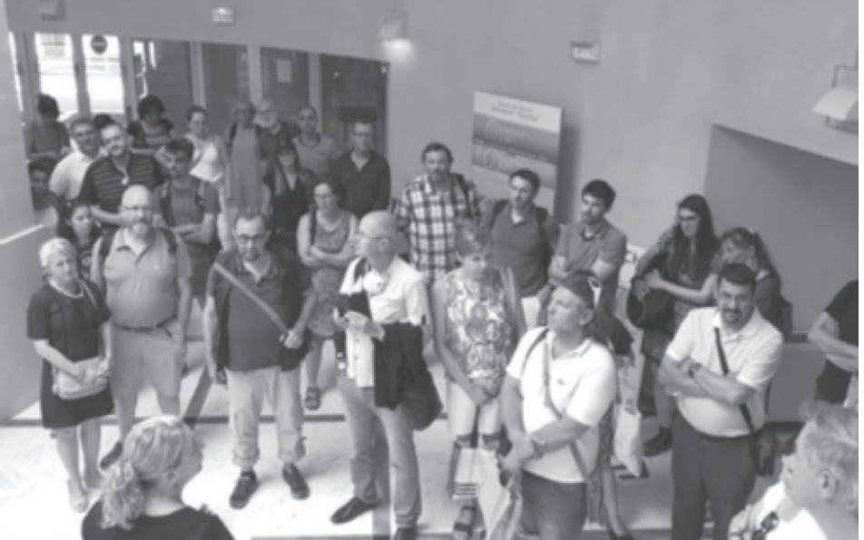 Description de l'image par IA : Groupe de personnes dans une salle, certaines avec des cannes, écoutant un orateur.