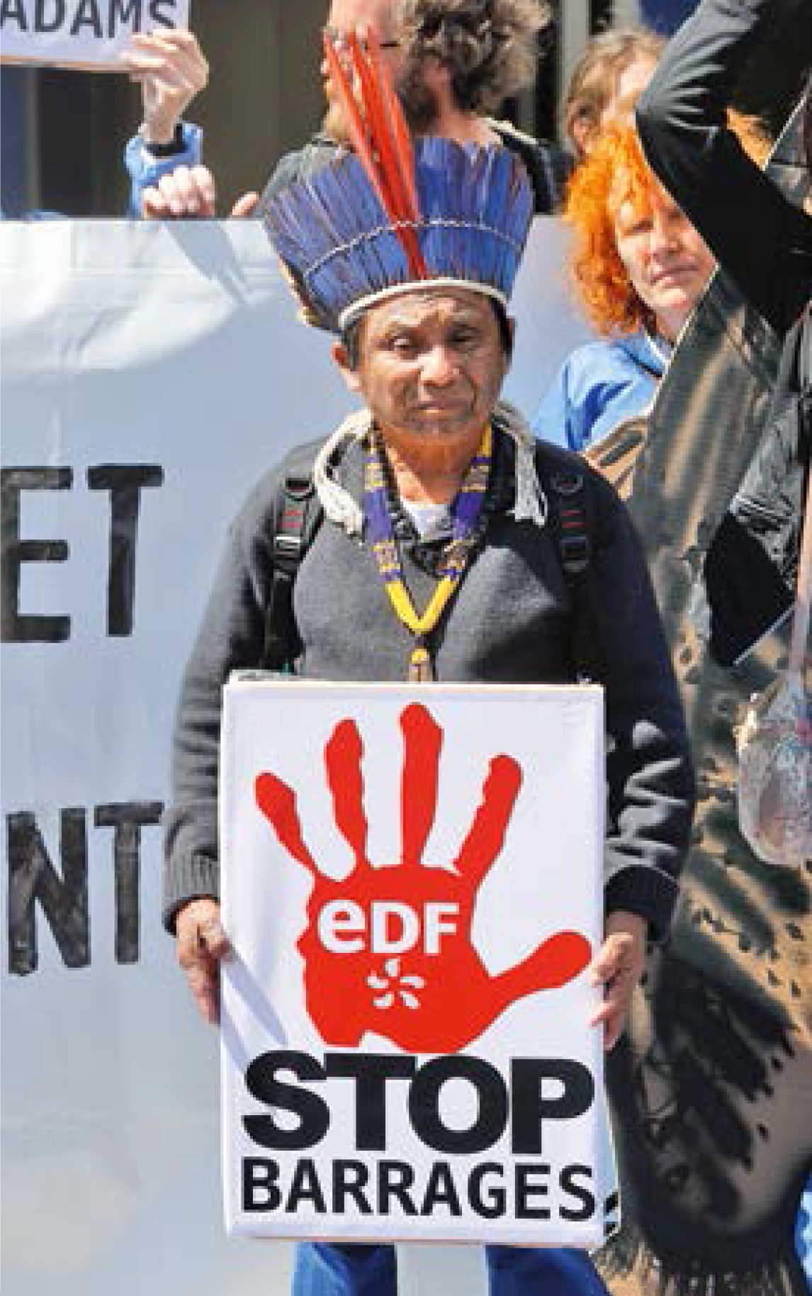 Description de l'image par IA : Personne tenant une pancarte "EDF STOP BARRAGES" lors d'une manifestation.