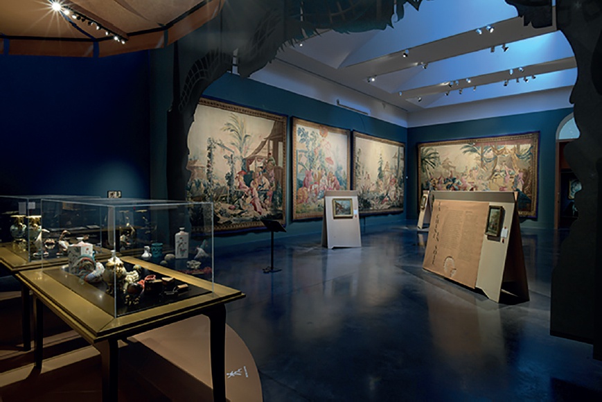 Description de l'image par IA : Salle d'exposition avec tapisseries et vitrines, éclairage bleu.