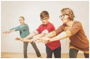 Description de l'image par IA : Trois personnes, dont deux adultes et un enfant, dansent ensemble dans une pièce. Elles sont en ligne, les bras tendus, souriantes.