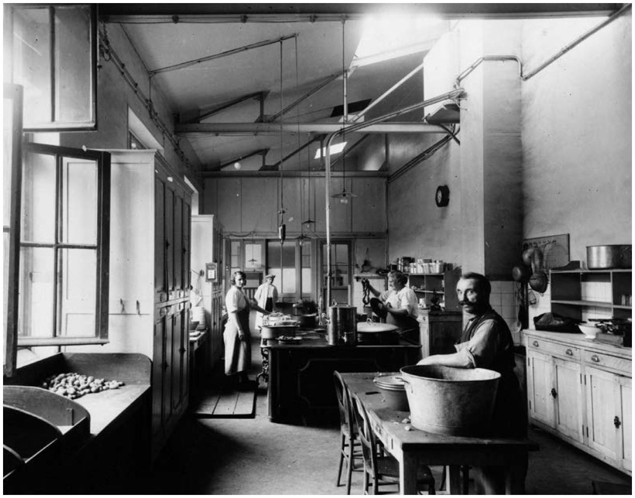 Description de l'image par IA : Cuisine industrielle avec plusieurs personnes travaillant. Un homme mélange dans un grand récipient, d'autres opèrent des machines.