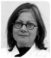 Description de l'image par IA : Photo en noir et blanc d'une femme aux cheveux mi-longs, portant des lunettes et un collier. Elle sourit légèrement.