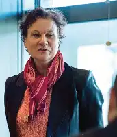 Description de l'image par IA : Femme âgée avec foulard rouge, veste sombre, regardant sérieusement.