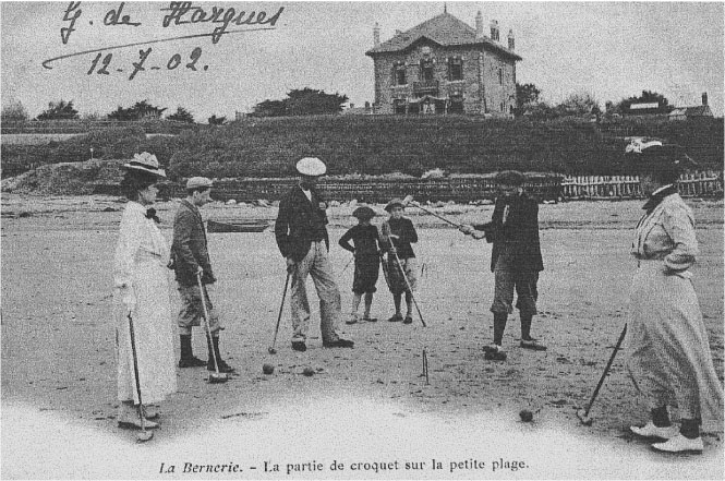 Description de l'image par IA : Huit personnes jouent au croquet sur une plage, avec une maison en arrière-plan.