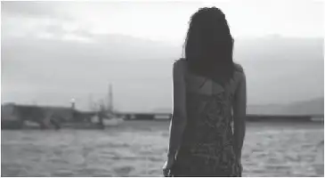 Description de l'image par IA : Femme dos tourné, près de l'eau, bateaux au loin.