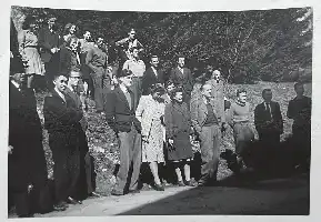 Description de l'image par IA : Groupe de personnes en extérieur, certains debout, d'autres assis. Homme en première rangée, quatrième de gauche, et sa femme.